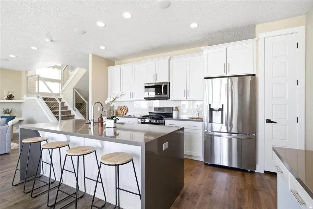 Kitchen featuring a large central island with seating, stainless steel appliances, white cabinetry, and wood-finish flooring