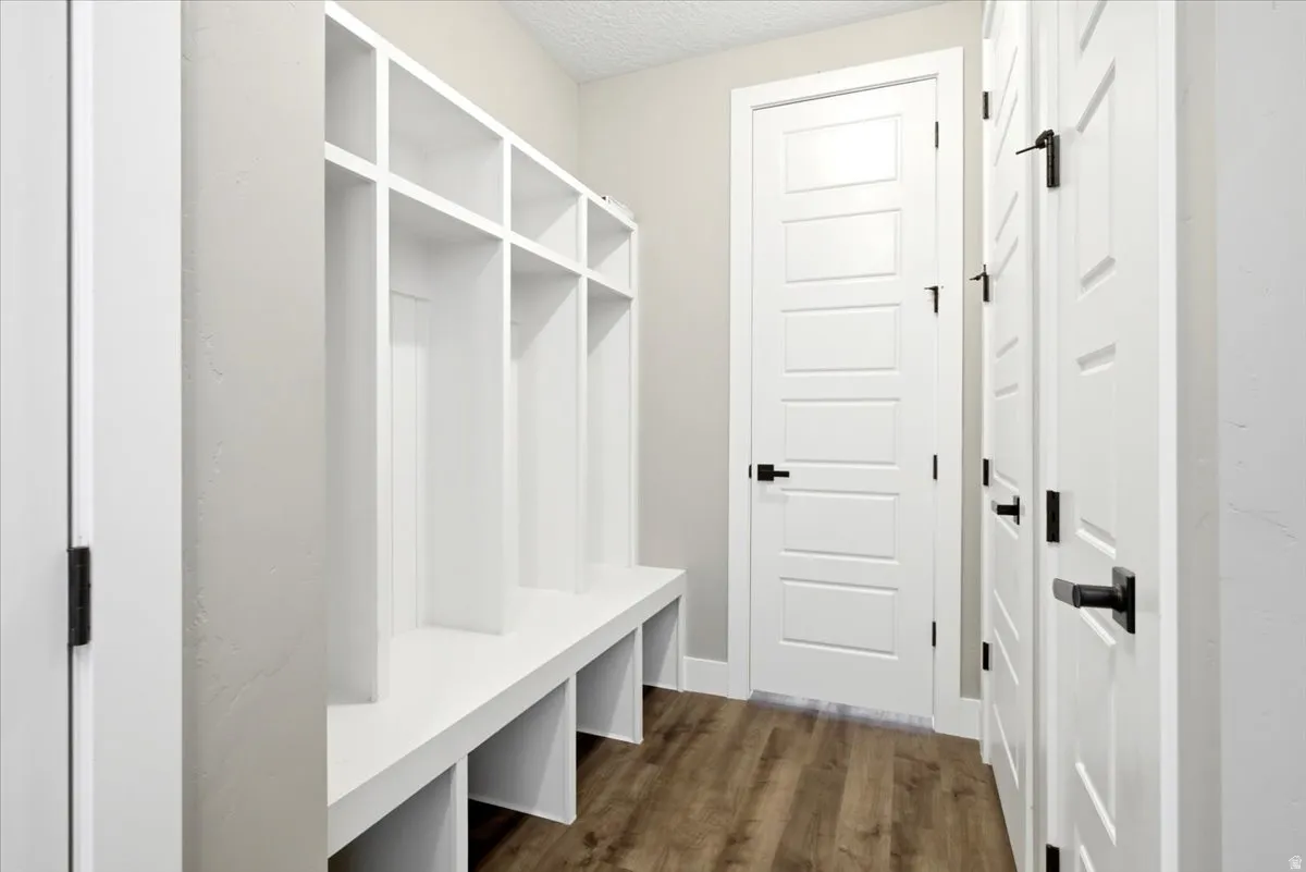 Mudroom featuring built-in white storage cubbies, a coordinating bench, wood-finish flooring, and crisp white paneled doors with matte black hardware