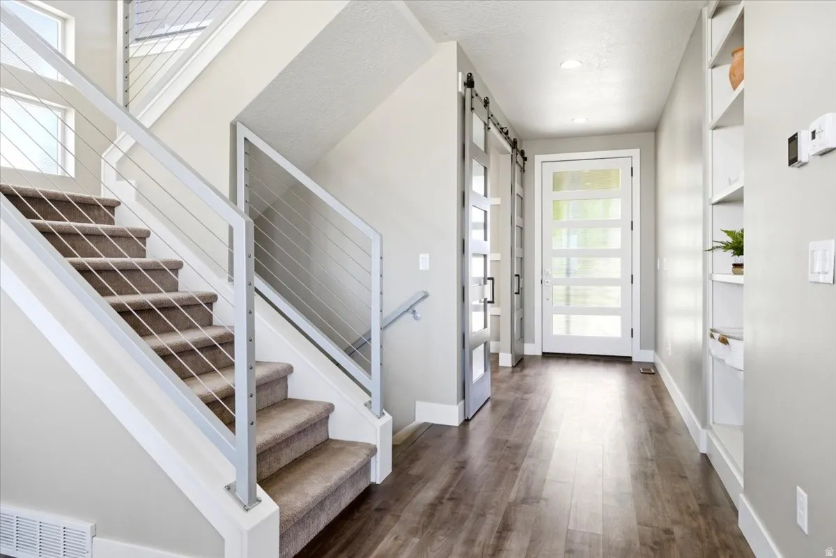 Carpeted staircase with modern cable railing, wood-finish flooring, built-in shelving, and contemporary paneled glass door