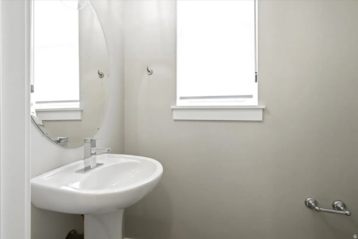 Pedestal sink with chrome faucet, complemented by a frameless oval mirror