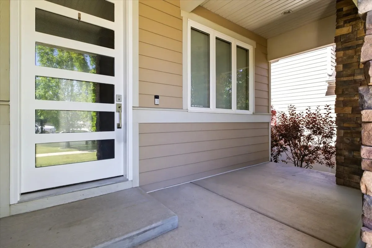 Inviting covered front porch entry featuring a modern white door with horizontal glass inserts, beige siding, and a stone-clad column