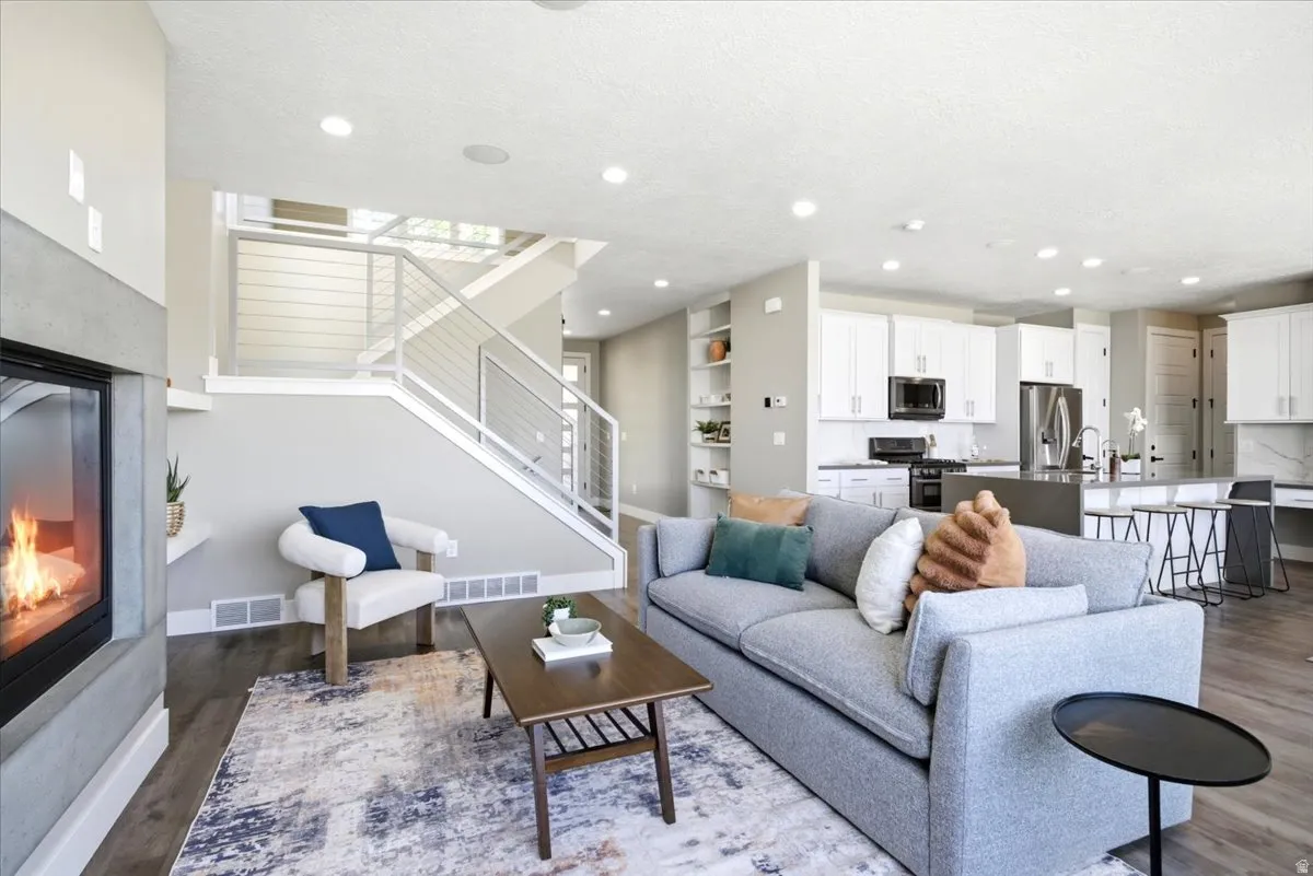 Open-concept living space featuring a modern fireplace with a concrete surround, wood-finish flooring, and recessed lighting