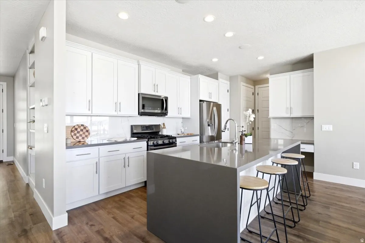 Kitchen featuring an extended island with seating, white shaker cabinetry, stainless steel appliances, and wood-finish flooring