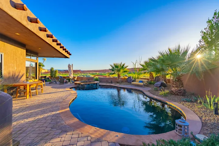 Curved swimming pool featuring an integrated hot tub and stone surround, set within a paver patio