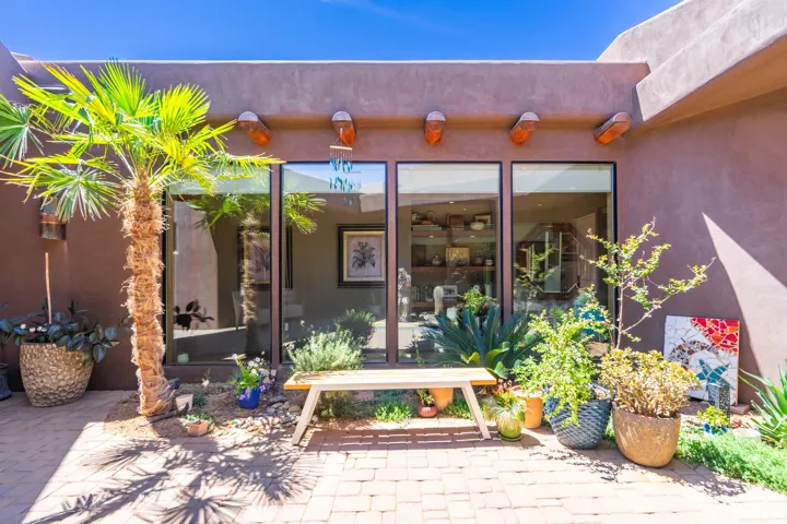 Paved patio featuring a stucco exterior with decorative corbels, large floor-to-ceiling windows, and surrounding desert landscaping
