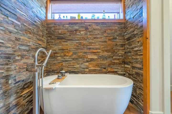 Freestanding soaking tub with a floor-mounted chrome faucet, set against textured stacked stone walls