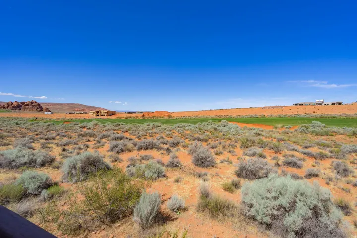Expansive desert landscape featuring natural brush, red-earth terrain, and a distant green golf course