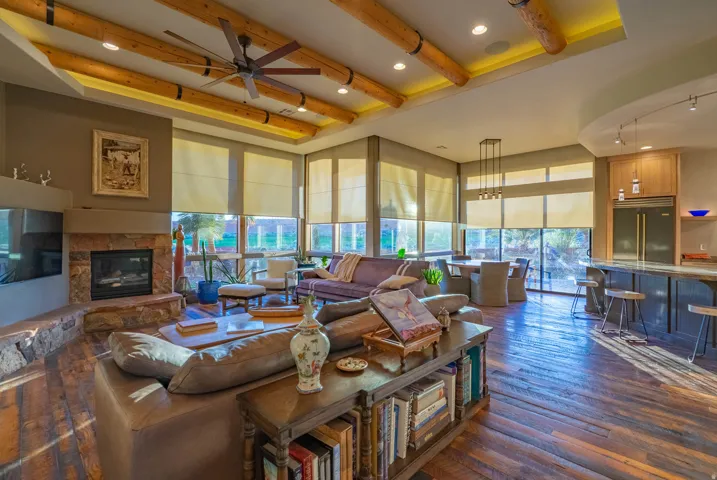 Spacious open-concept living area featuring wood-finish flooring, a stone-faced fireplace with hearth, and a wood beam ceiling with recessed lighting