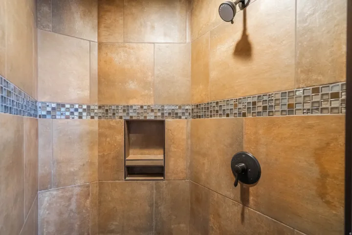 Shower featuring large format tile, mosaic tile accent band, built-in recessed niche, and dark bronze fixtures