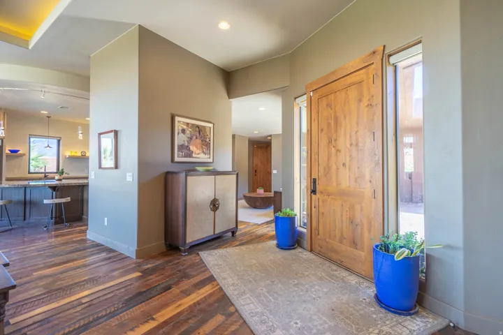 Solid wood entry door with vertical sidelight windows, wood-finish flooring, recessed lighting, and a partial view of a kitchen with an island