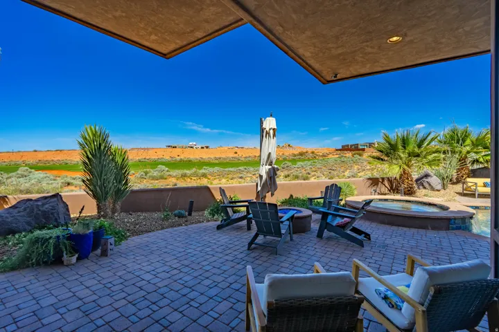 Expansive paver patio with a built-in hot tub, integrated fire pit, and surrounding desert landscape