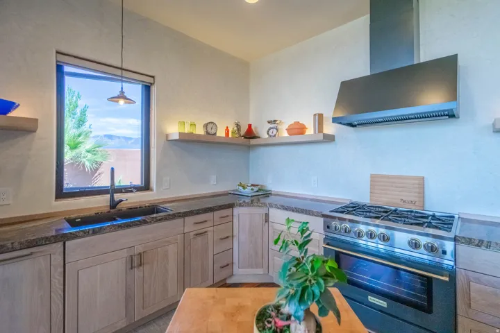 Kitchen featuring light wood-finish cabinetry, granite countertops, a stainless steel gas range with a coordinating range hood, and a black sink with a contemporary faucet