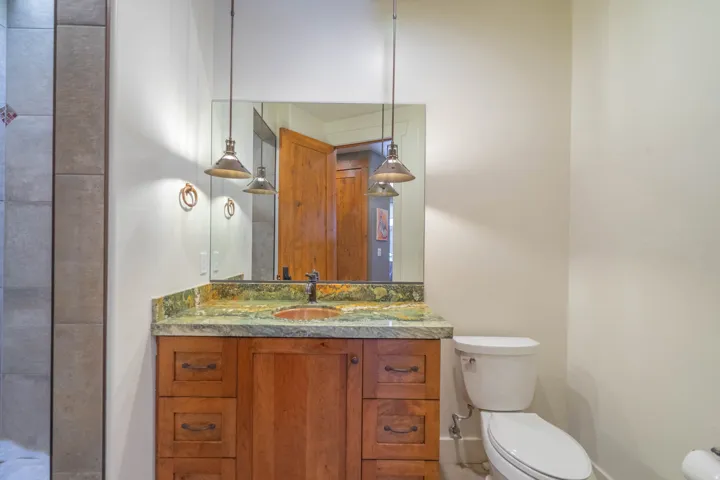 Wood-finish vanity with drawer and cabinet storage, green variegated countertop, and a copper-toned basin