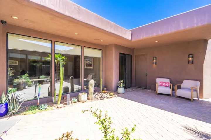 Expansive paver patio with a desert-inspired landscape border, three large picture windows, and recessed lighting