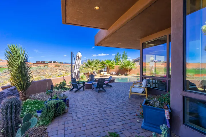 Expansive paver patio with a built-in fire pit, surrounded by desert landscaping and mature palm trees
