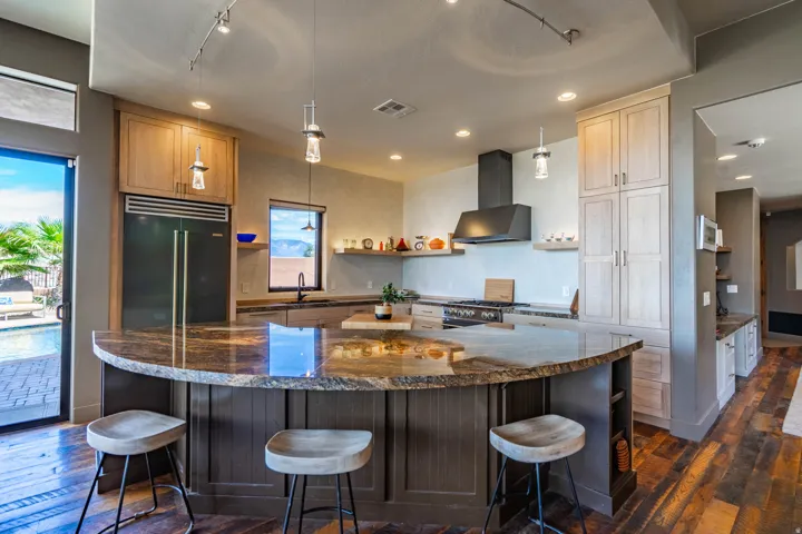 Kitchen featuring a large curved island with a stone countertop and seating, wood-finish flooring, a stainless steel refrigerator, and a dark range hood