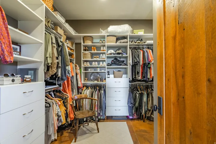 Walk-in closet featuring extensive built-in shelving, multiple hanging rods, integrated drawer storage, and warm wood-finish flooring