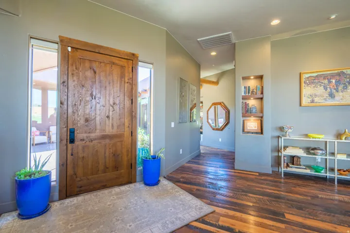 Solid wood entry door with vertical paneling, sidelight windows, wood-finish flooring, an illuminated built-in display niche, and recessed ceiling lighting