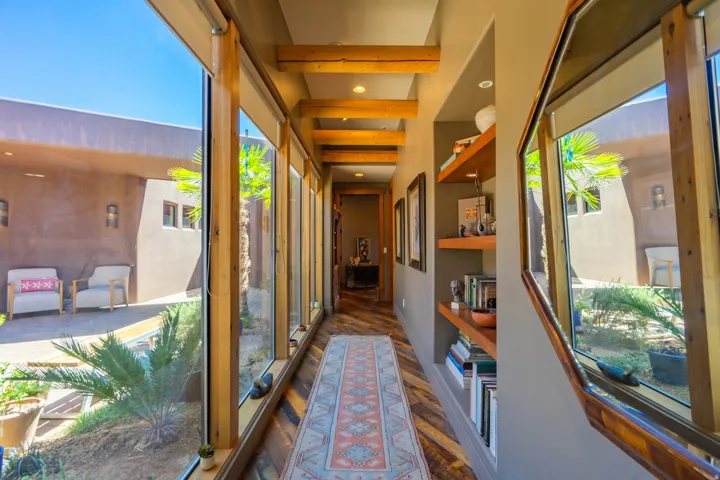 Hallway with exposed wood beams, wood-finish flooring, built-in shelving, and a wall of windows overlooking a courtyard