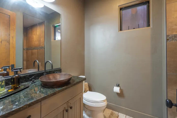 Bathroom vanity featuring a copper vessel sink, dark stone countertop, and black fixtures