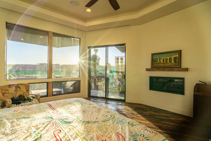 Expansive window wall with a sliding glass door, rich wood-finish flooring, recessed lighting, ceiling fan, and a built-in fireplace with a floating mantel