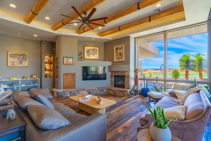 Spacious living area featuring exposed wood beam ceilings with recessed lighting, an integrated stone fireplace with a raised hearth, and wood-finish flooring