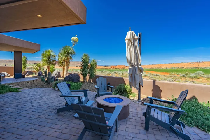 Spacious paver patio featuring a built-in fire pit with blue glass, desert landscaping, and privacy wall