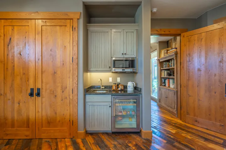 Wet bar featuring light-colored cabinetry, an integrated microwave, a stainless steel under-counter beverage refrigerator, a sink with a stainless steel faucet, and dark countertops
