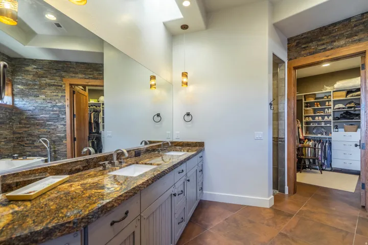 Dual vanity with a stone countertop and under-mount sinks, illuminated by pendant lights