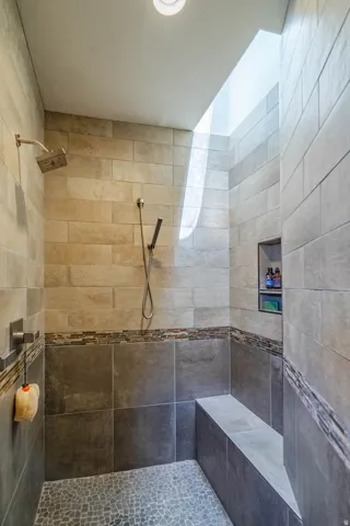 Walk-in shower featuring a pebble-tiled floor, a built-in bench, and a skylight