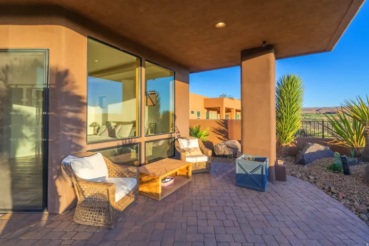 Shaded outdoor patio featuring paver flooring, a stucco exterior, expansive windows, and desert landscaping