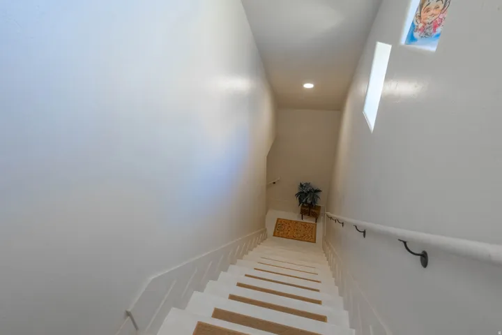 Staircase featuring white risers, carpeted treads, and a white handrail with dark metal brackets