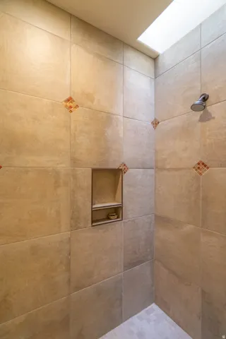 Tiled shower enclosure featuring a skylight, a built-in shower niche with shelving, and decorative accent tiles