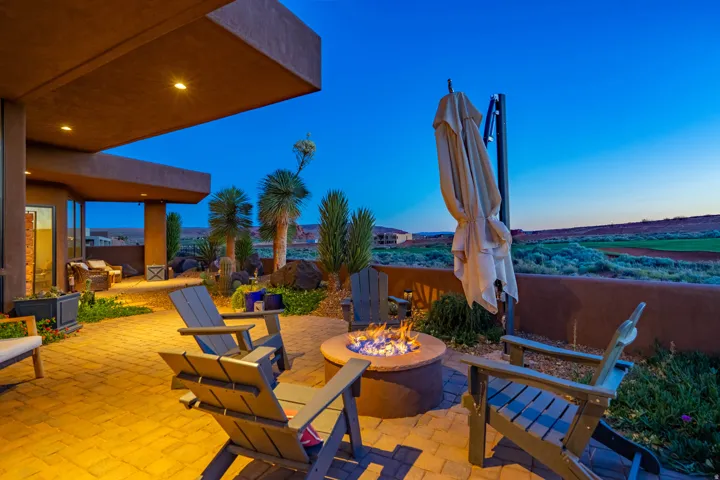 Expansive paver patio with a built-in fire pit, surrounded by desert landscaping and a low perimeter wall