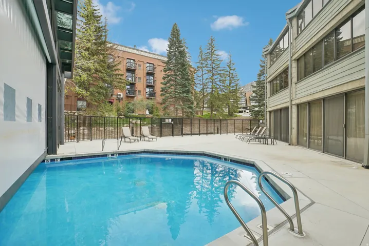 Outdoor swimming pool with concrete decking, surrounded by a black metal fence