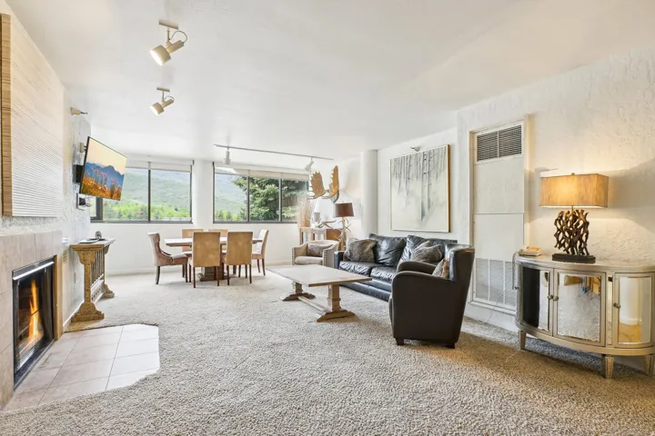 Open-concept living area featuring a stone-clad fireplace with a tiled hearth, track lighting, and expansive windows