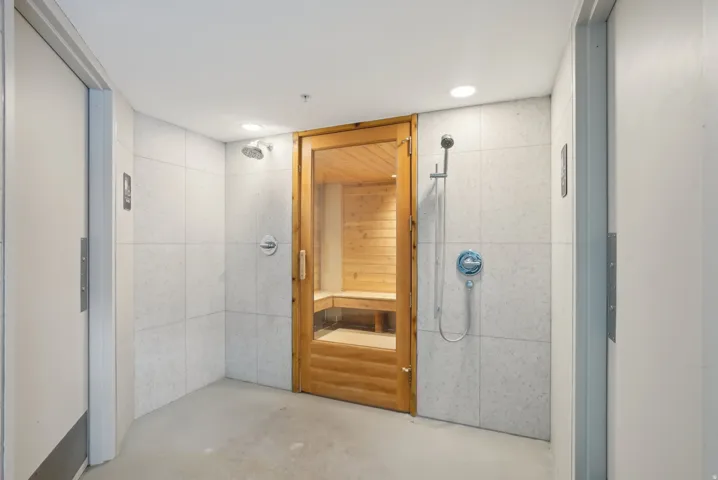 Indoor sauna with a clear-paneled wooden door, flanked by two shower areas featuring light-toned tile walls and chrome fixtures