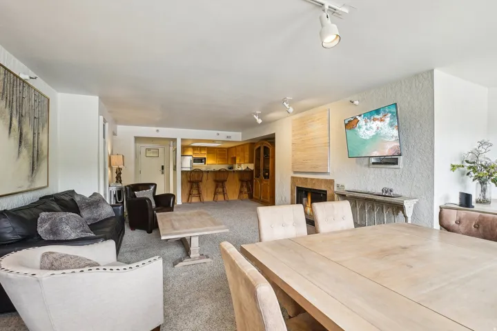 Open-concept living space featuring a dining area with a light wood-finish table, track lighting, a textured wall finish, and a built-in fireplace with a stone surround