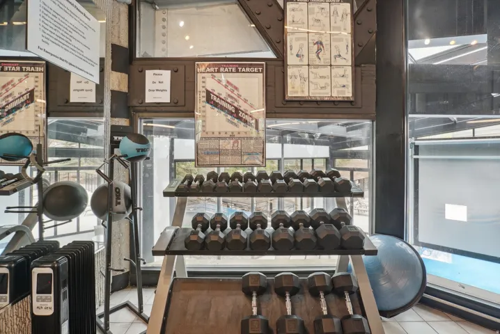 Dedicated fitness area featuring a comprehensive dumbbell rack, ample natural light, and structural beams