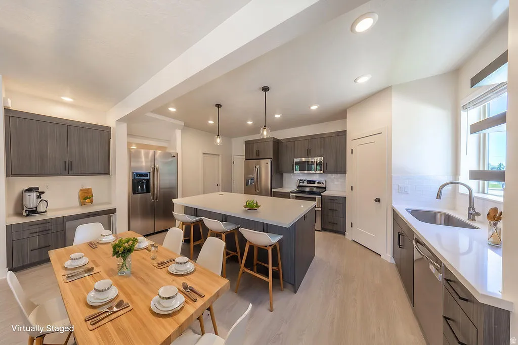 Virtually Staged. Open-concept kitchen featuring an oversized island with seating, stainless steel appliances, grey wood-finish cabinetry, white countertops, and light wood-finish flooring