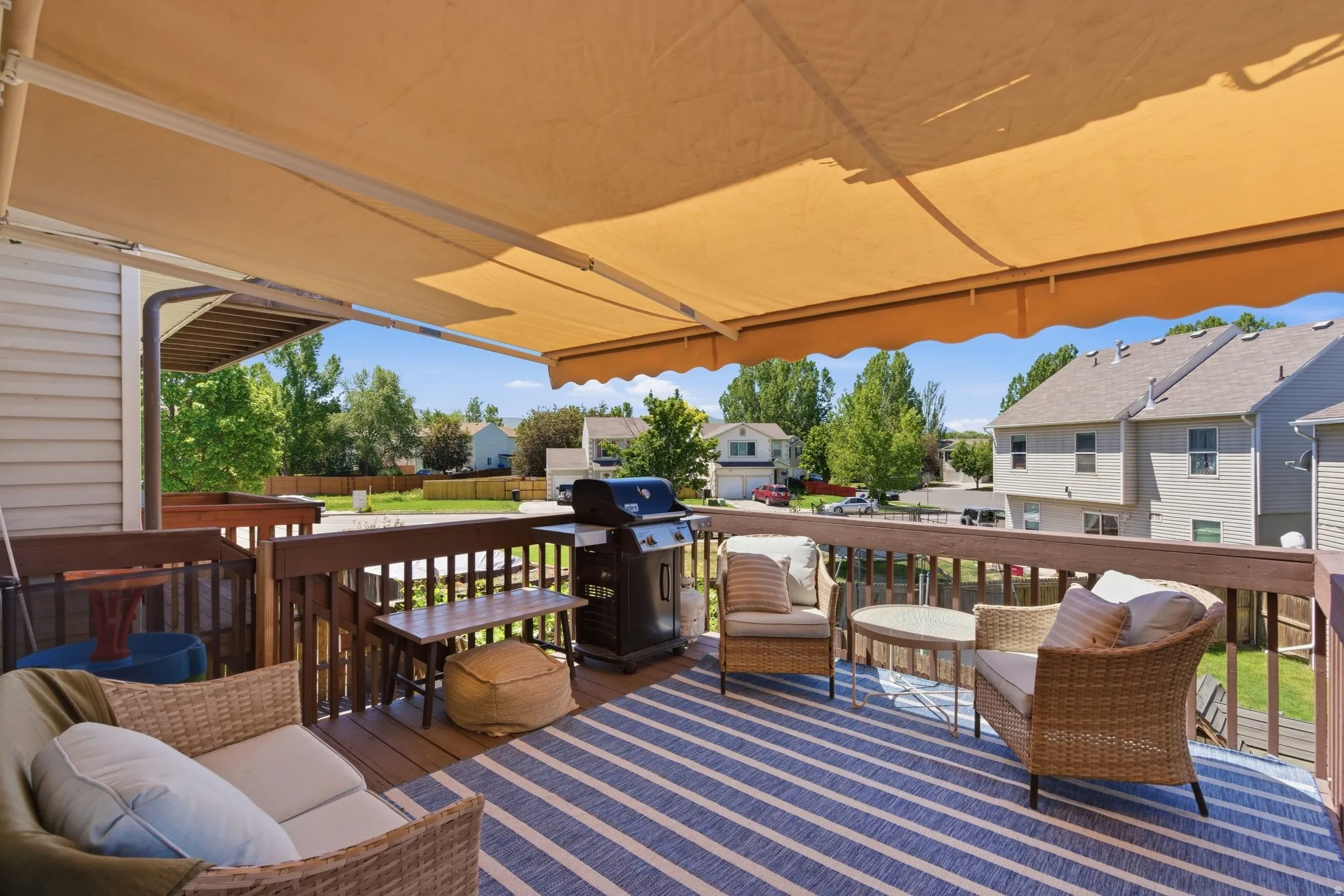 Expansive outdoor deck featuring wood flooring, a decorative striped rug, and a retractable awning for shade
