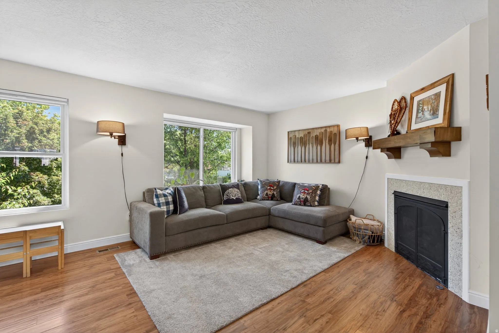Living space featuring wood-finish flooring, a fireplace with a light-colored surround and dark metal insert, and an overhead wooden mantel