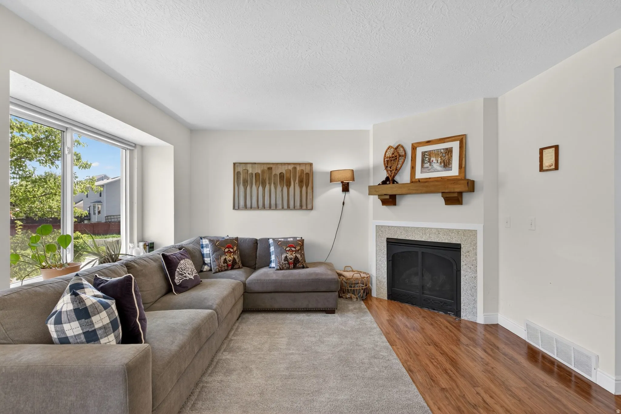 Living area with a large picture window and a fireplace featuring a wooden mantel and stone surround