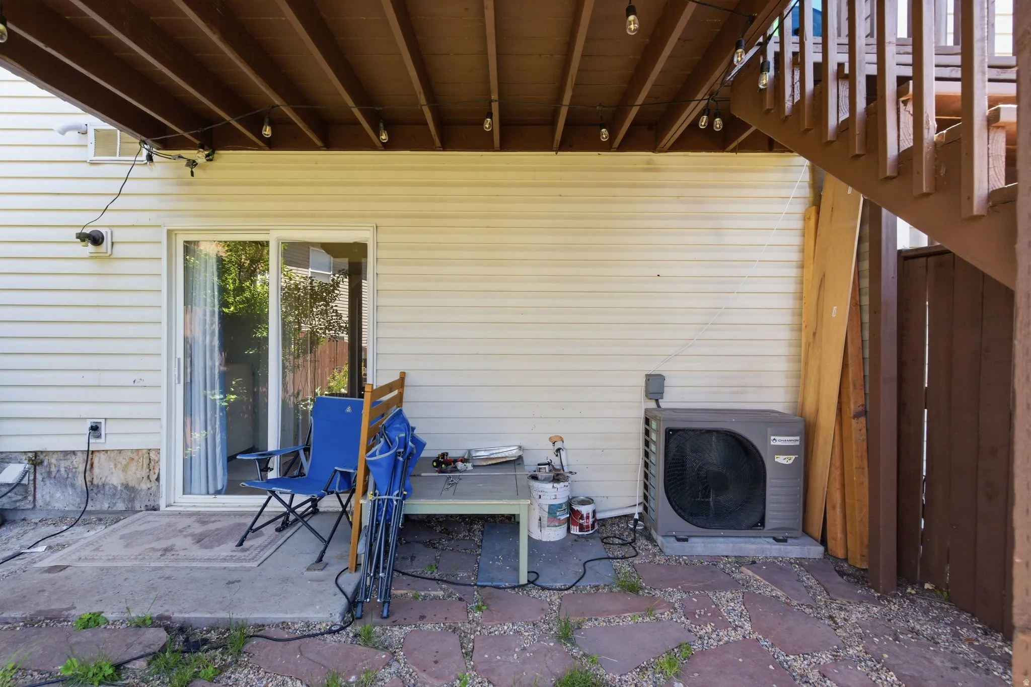 Lower-level patio area featuring a sliding glass door entry, stone paver ground covering, and a partial privacy fence