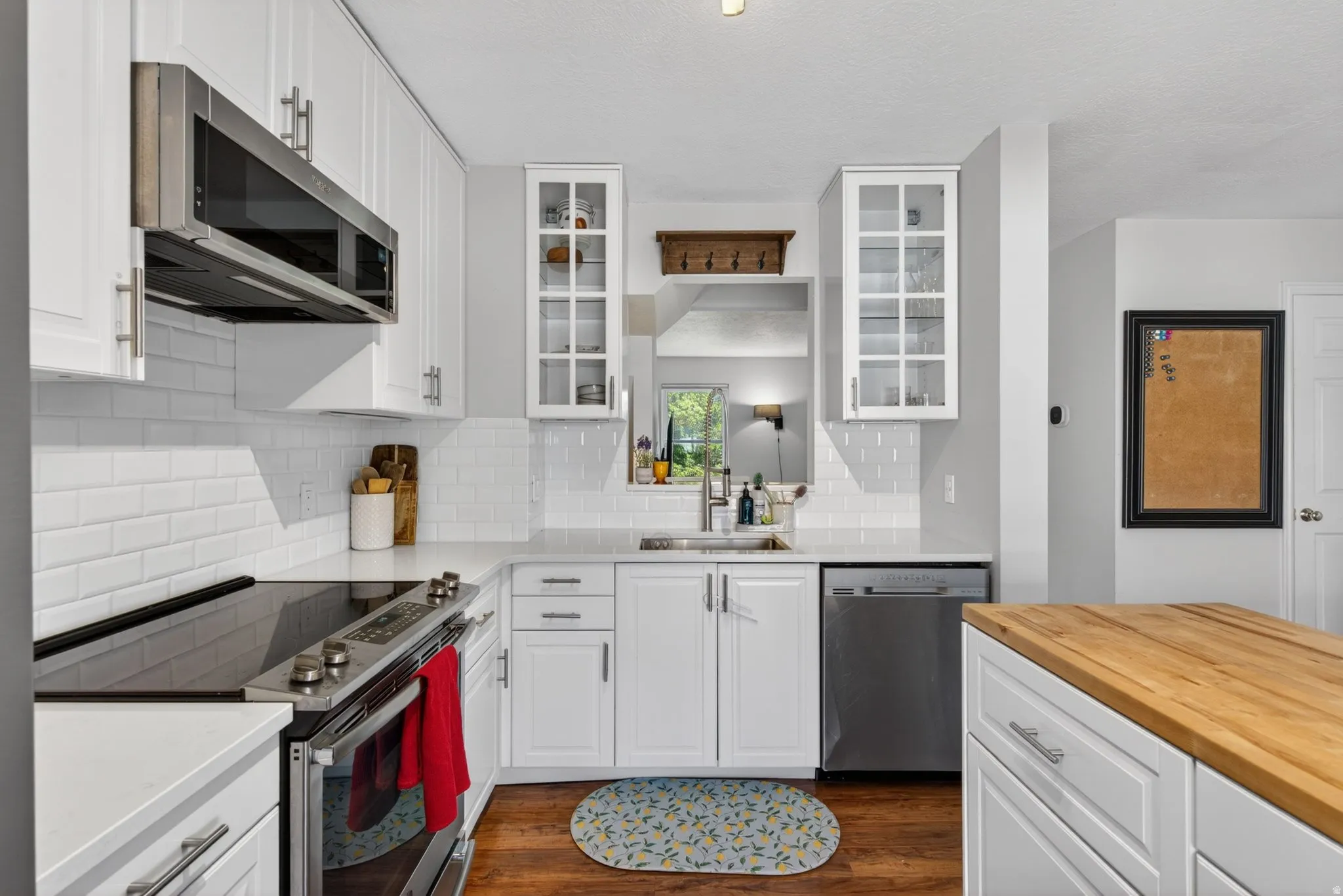 White cabinetry with brushed nickel hardware, stainless steel appliances, white subway tile backsplash, and wood-finish flooring