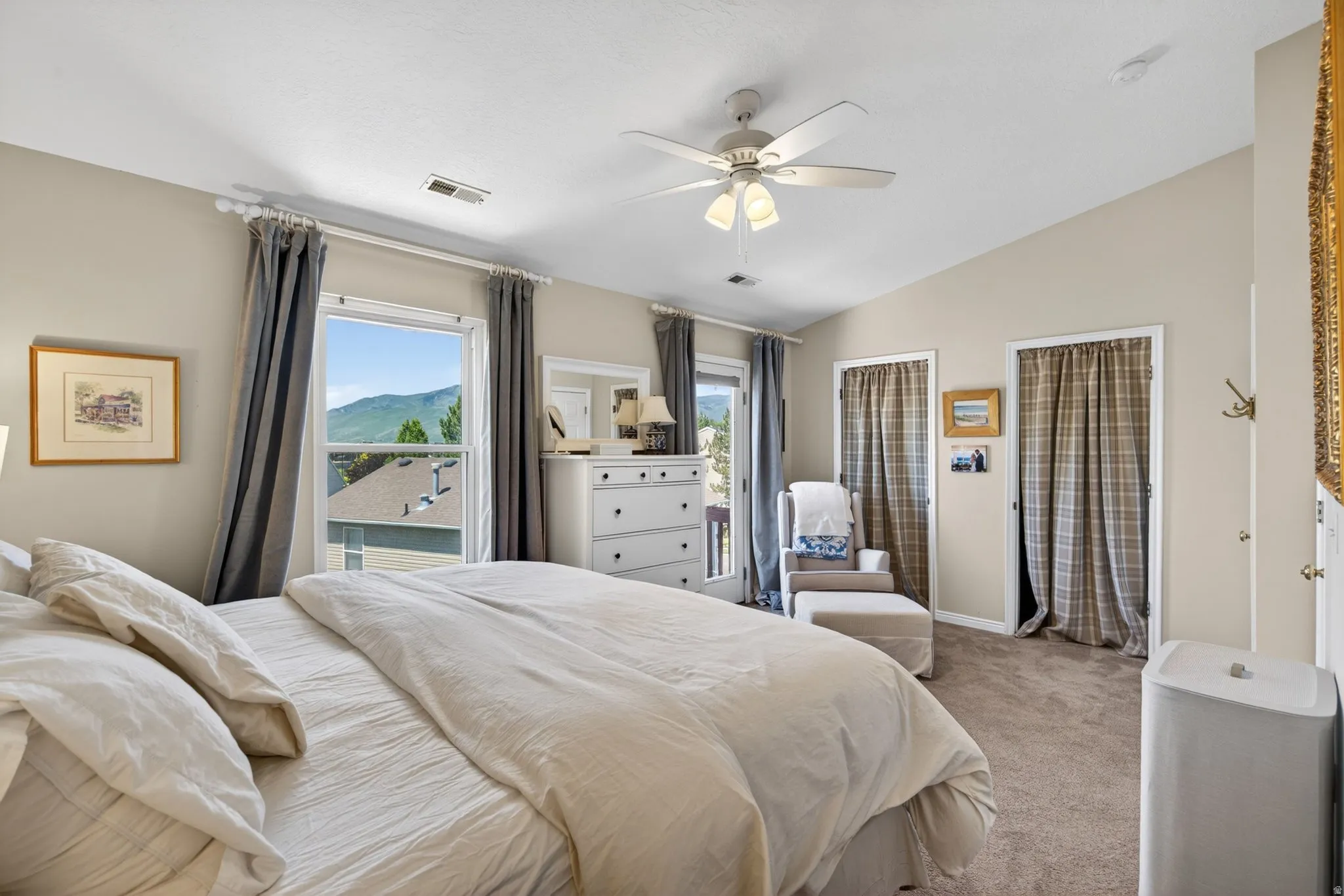 Carpeted bedroom featuring vaulted ceilings, a ceiling fan with light fixture, multiple windows, and a glass-paneled door