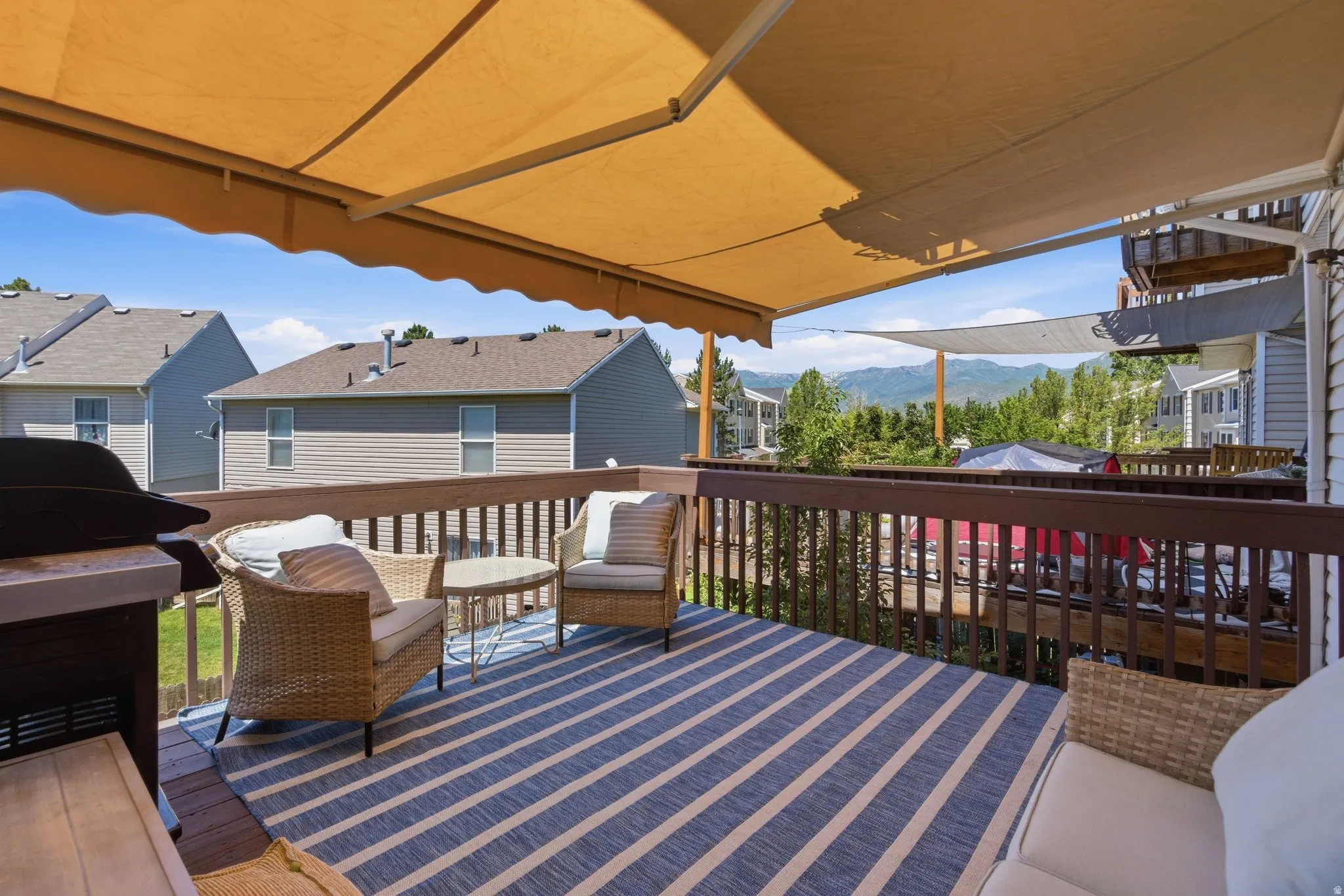 Expansive outdoor deck featuring a retractable awning, dark wood railing, and mountain scenery