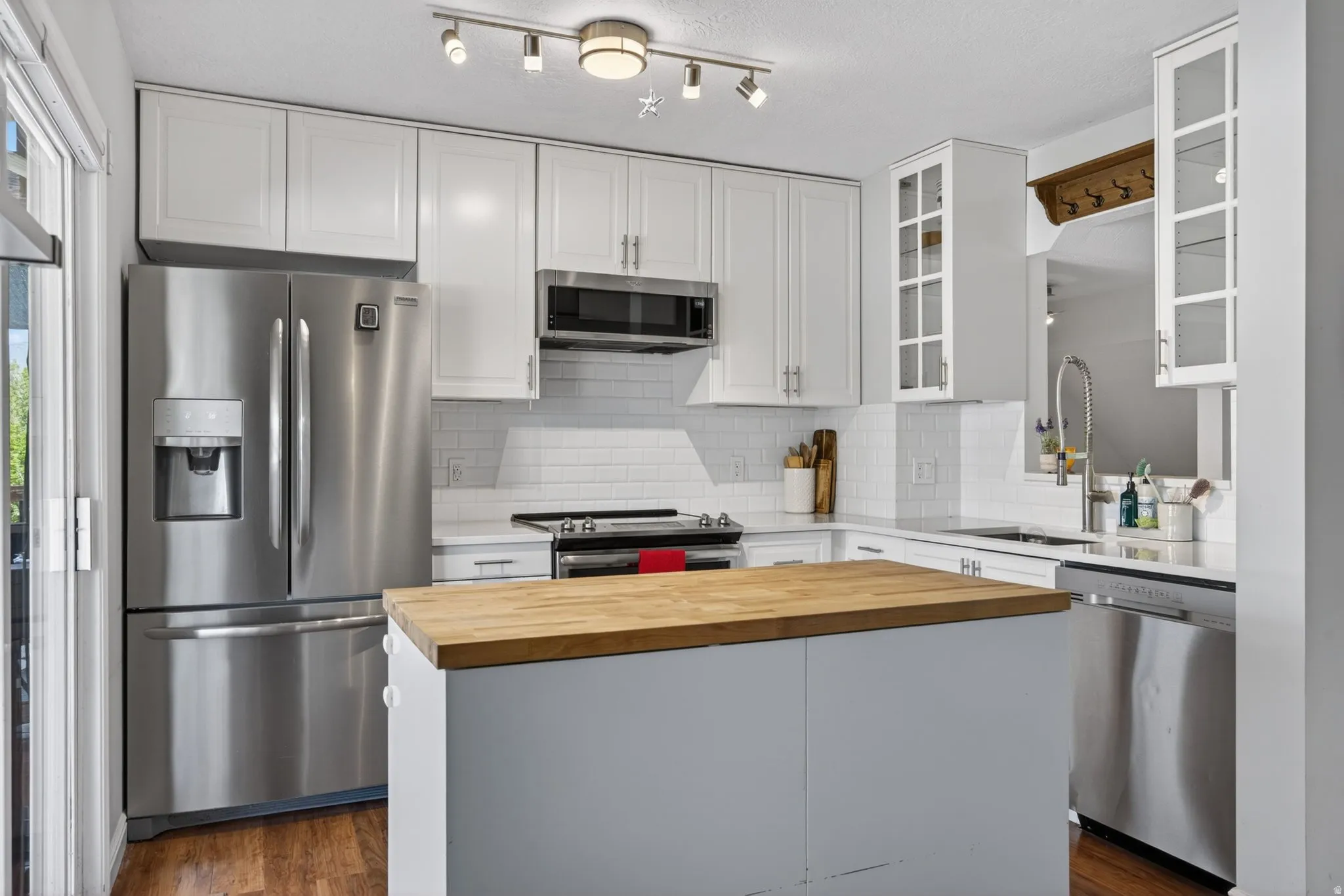 Contemporary kitchen featuring white cabinetry, stainless steel appliances, butcher block island, white subway tile backsplash, and wood-finish flooring