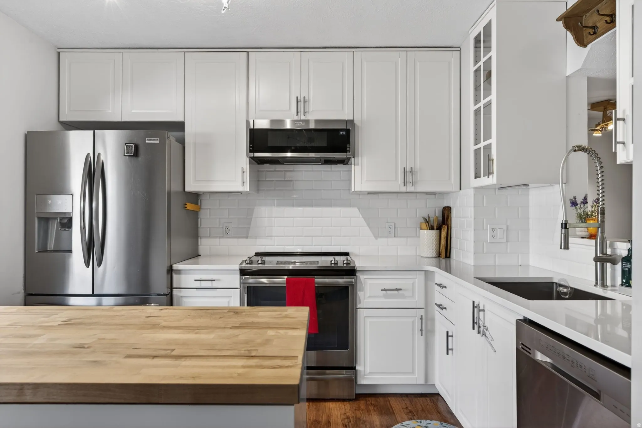 Kitchen featuring white shaker-style cabinetry, stainless steel appliances, white subway tile backsplash, light-toned countertops, and a wood-finish island countertop