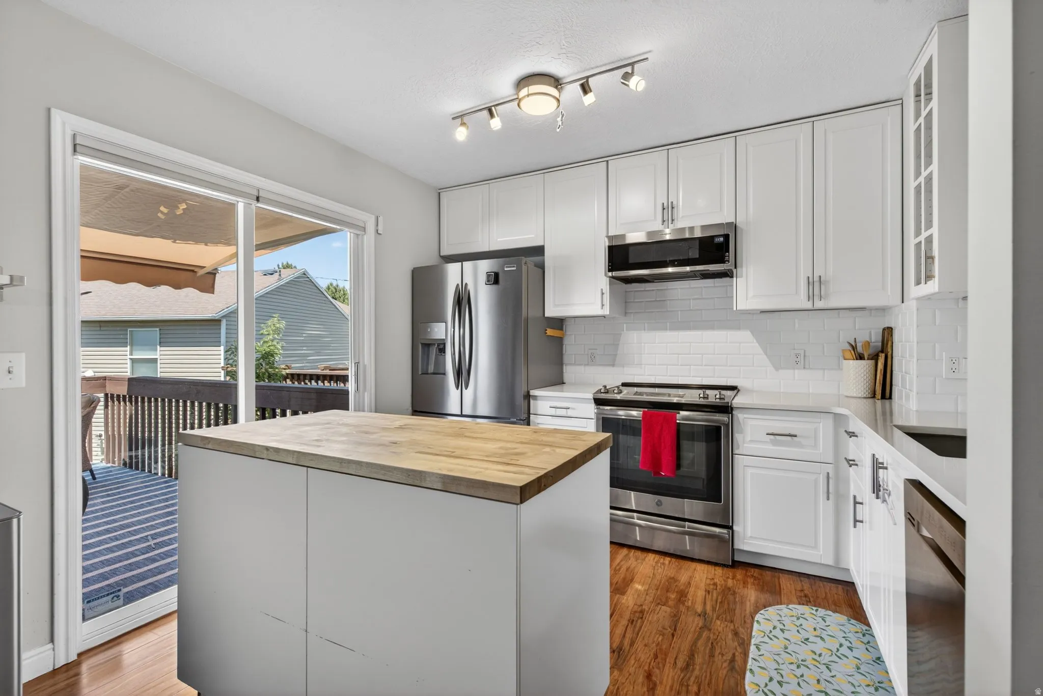 Contemporary kitchen featuring a center island with a wood-finish countertop, white cabinetry, stainless steel appliances, a subway tile backsplash, and wood-finish flooring